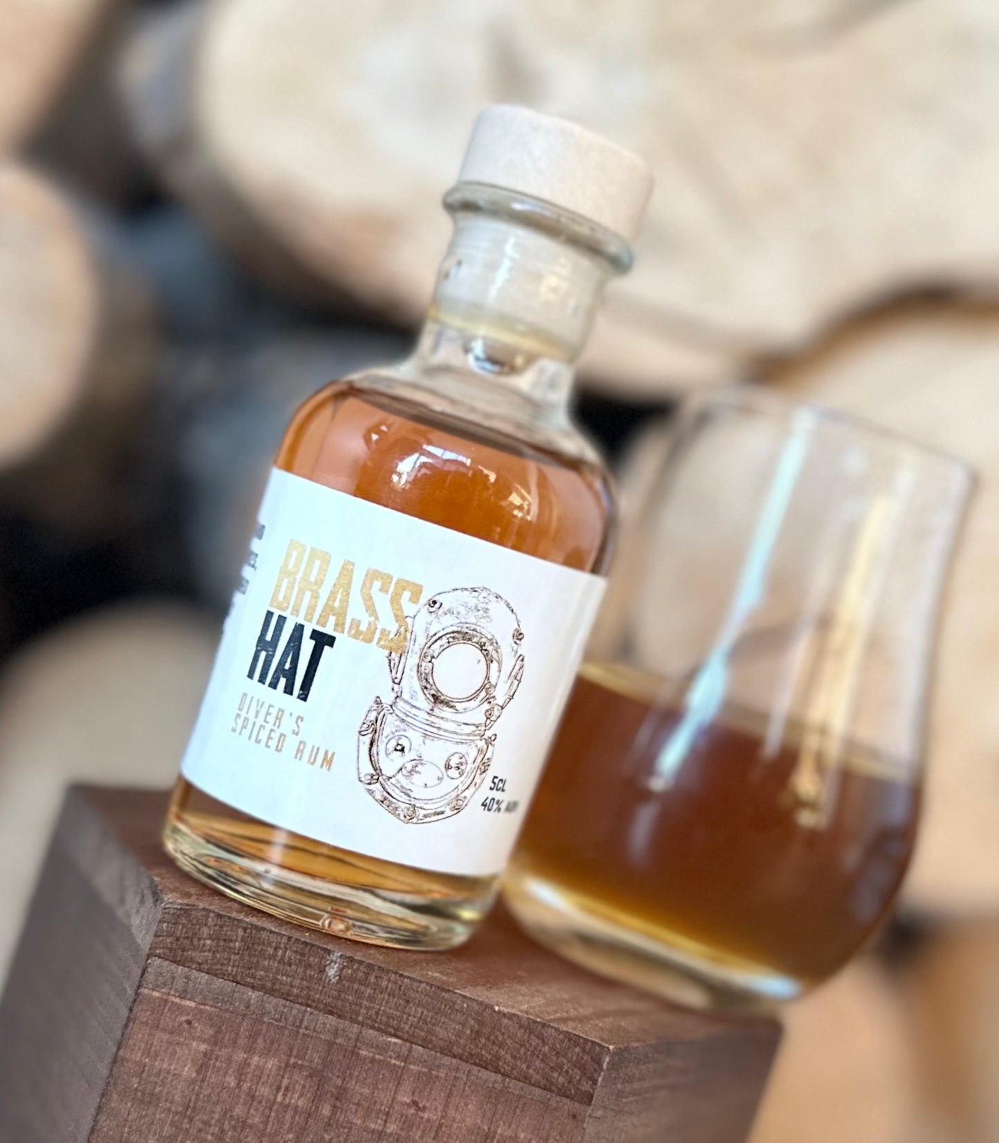 Miniature bottle of brass hat diver’s spiced rum sat on a wooden display shelf next to a snifter glass of rum