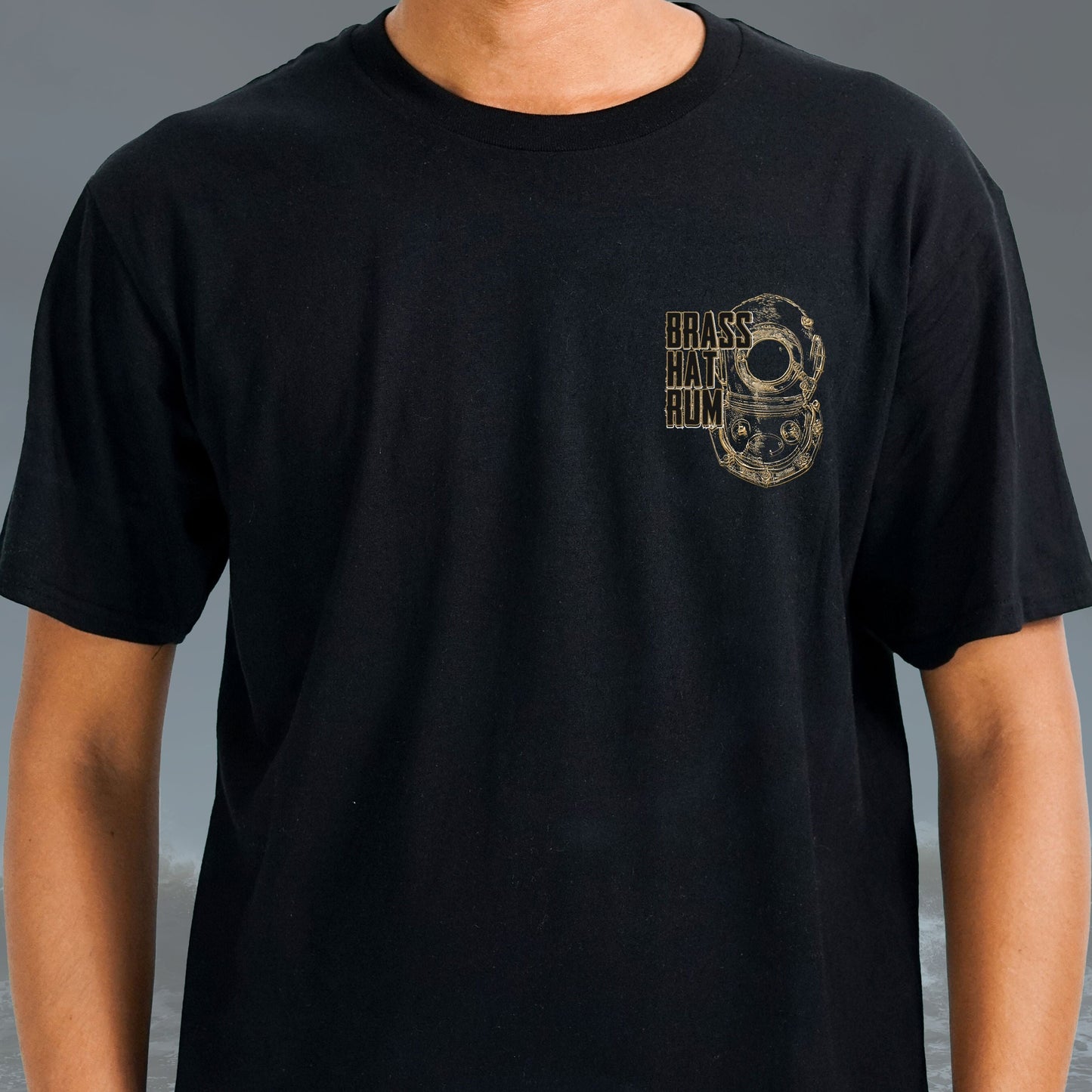 Front view of person wearing Brass Hat Rum black round-neck t-shirt. Deep sea diving helmet logo on left chest – divers’ gifts and ocean-inspired apparel
