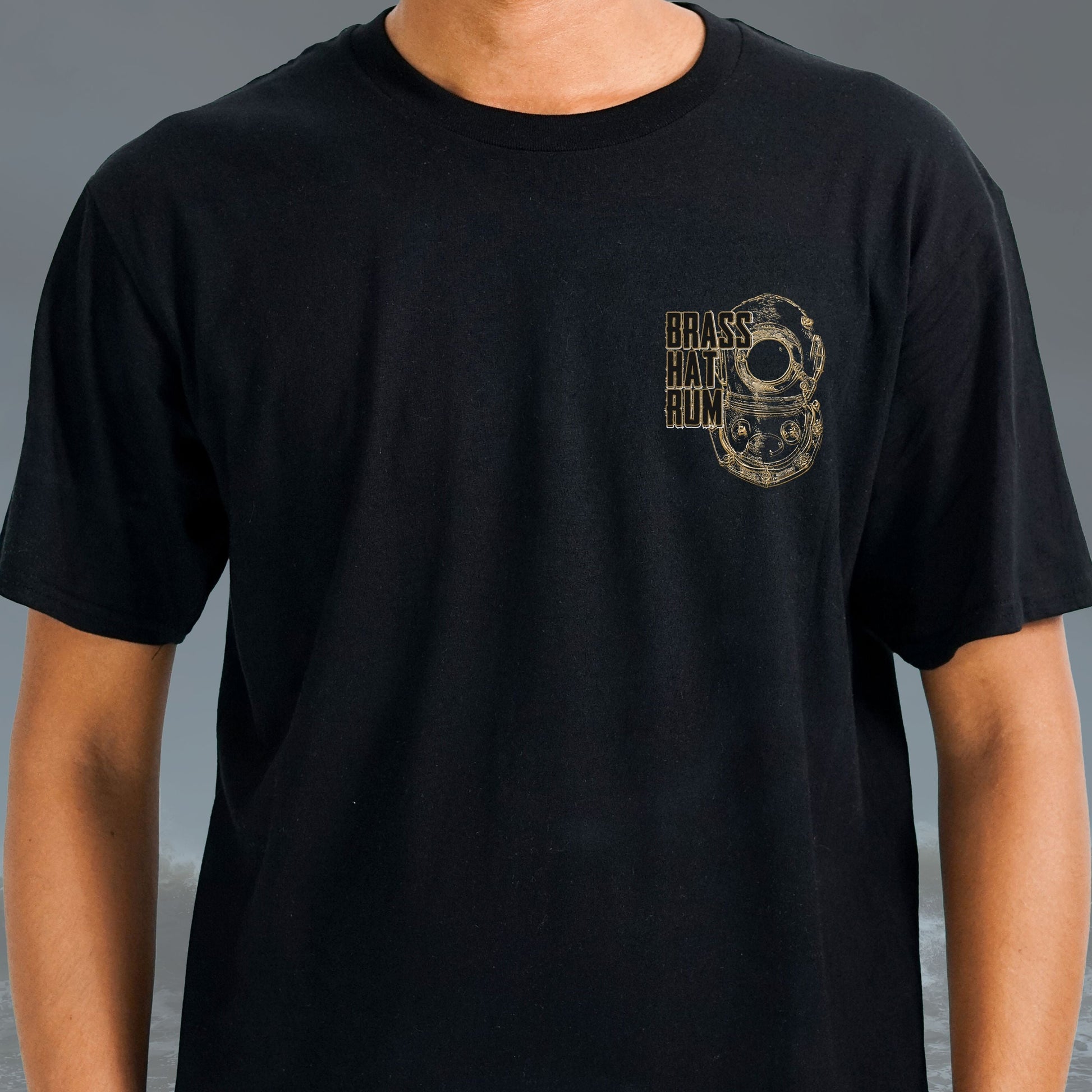 Front view of person wearing Brass Hat Rum black round-neck t-shirt. Deep sea diving helmet logo on left chest – divers’ gifts and ocean-inspired apparel